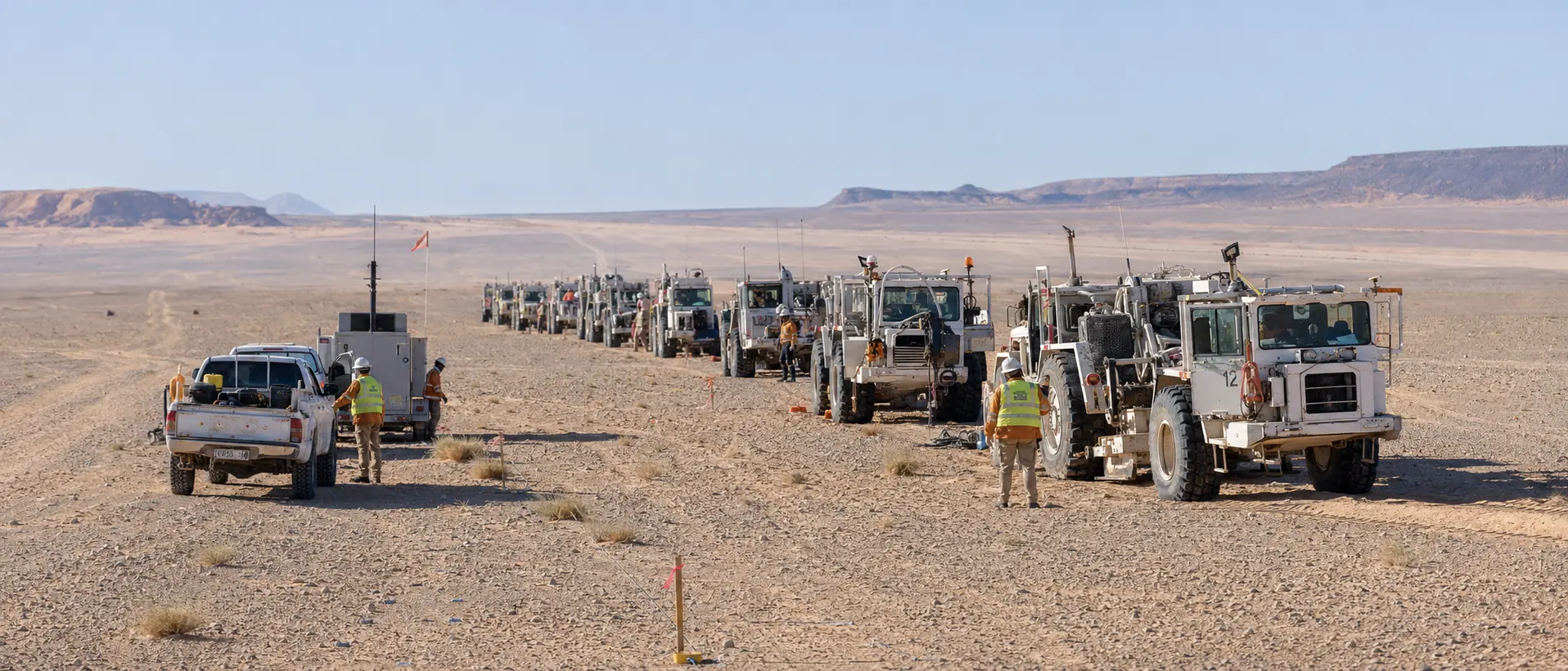 A NAGECO seismic crew: a line of vibroseis units, recording vehicles and field personnel in high-visibility clothing across open desert.